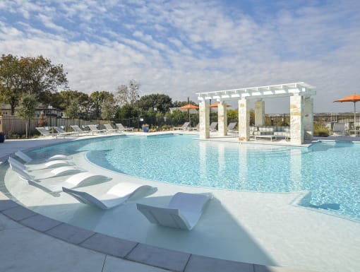 Resort-style swimming pool with in-water lounge chairs, shaded pergola seating, and a beautifully designed outdoor space.