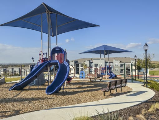 Community playground with modern equipment, shade structures, and nearby seating set within a landscaped residential area.