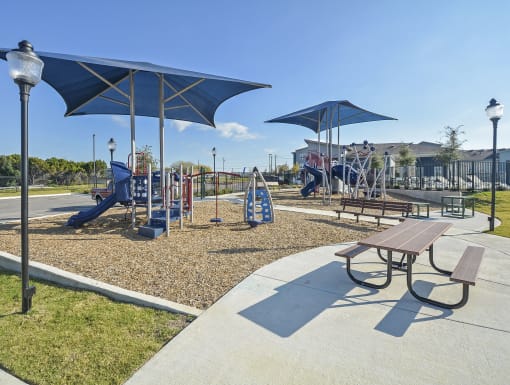 Community playground with modern equipment, shade structures, and nearby seating set within a landscaped residential area.