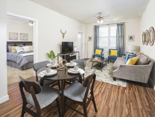 Open-concept living and dining area with modern furnishings, wood-style flooring, and a seamless view into a comfortable bedroom.