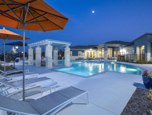 Inviting community pool with shallow tanning ledge, comfortable loungers, and a pergola-covered seating space.