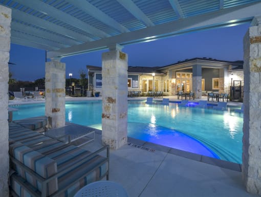 Inviting community pool with shallow tanning ledge, comfortable loungers, and a pergola-covered seating space.