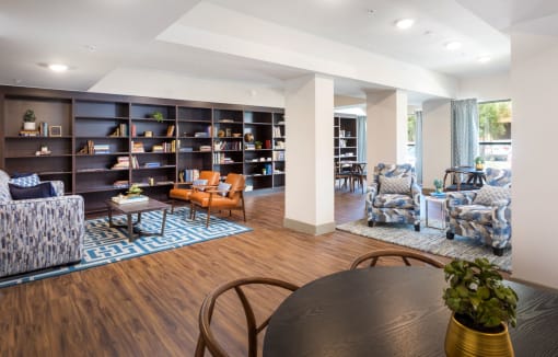 Springville Seniors Apartments community library with beautiful wall to wall dark brown shelving on one main wall, tables and chairs, couches and accent chairs