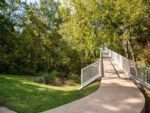 Curved walking path leading to pedestrian bridge at The Brook At Columbia Apartments, Columbia, Maryland