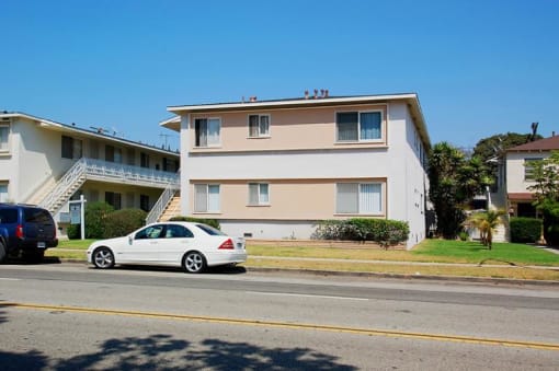A white car is parked on the side of the road in front of a two-story building.
