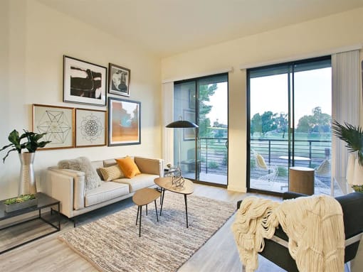 Luxury Apartments in Scottsdale AZ - Dusk Scottsdale - Living Room with Wood-Style Flooring, Couch, Chair, Coffee Table, End Tables, Lamp, Area Rug, Wall Art, and Sliding-Glass Doors to Patio