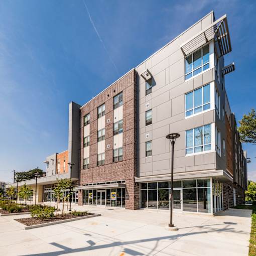 A modern building with a mix of brick and panel construction is shown under a clear blue sky.