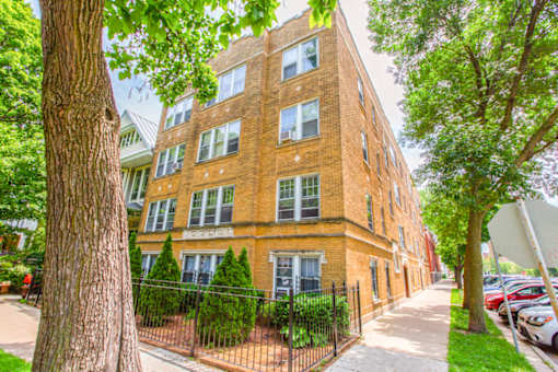 A red brick building with a black fence and green trees in front.