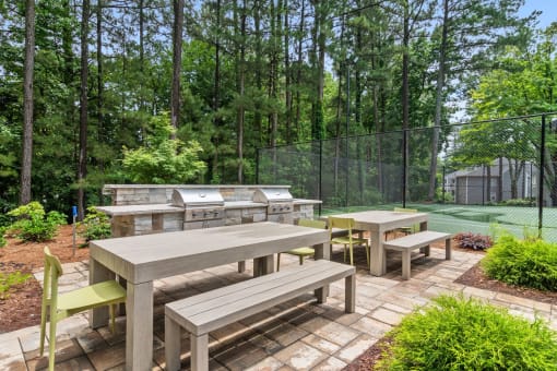 an outdoor patio with a picnic table and grill and a tennis court in the background