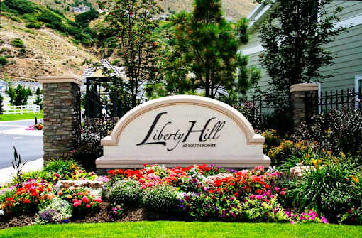 Stone entrance monument with colorful flower beds at Liberty Hill Apartments, Utah, 84020