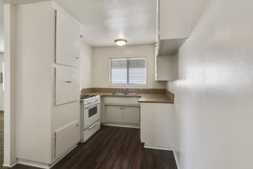 Kitchen with white gas range,  granite countertops, white cabinets, and wood-inspired floors