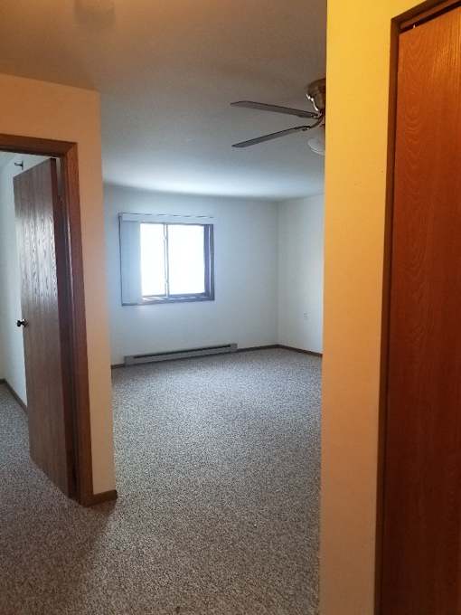 A room with a carpeted floor, a ceiling fan, and a window with blinds.