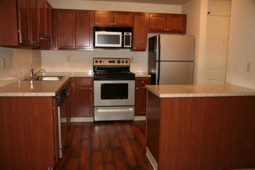a kitchen with brown wooden cabinets and stainless steel appliances at Heritage Grove Apartments in Renton, WA