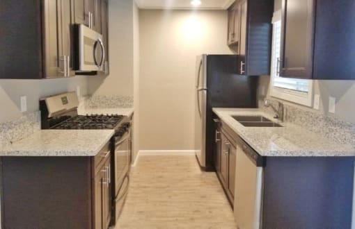 View of kitchen with stone counters, stainless appliances, brown cabinets, and wood look flooring