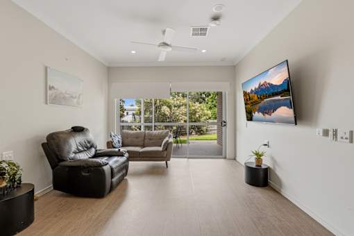 A living room with a black leather sofa and a flat screen TV mounted on the wall.
