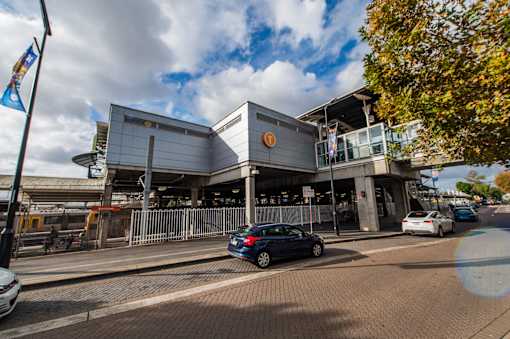A car is parked in front of a grey building with a circular logo on the top.