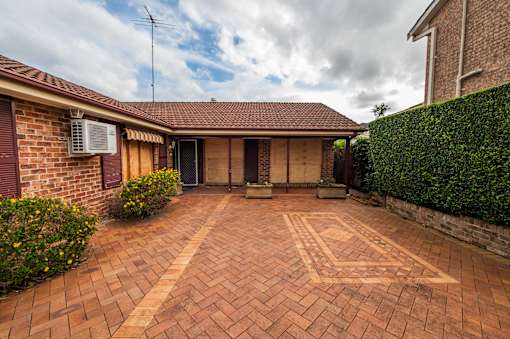 A brick patio with a pattern in the middle leads to a house.