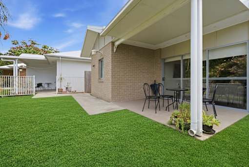 A house with a white fence and a patio with chairs and a table.