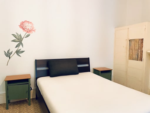 a small bedroom with a bed and a pink flower on the wall