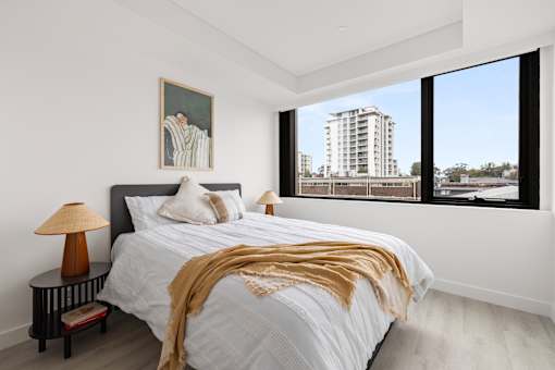 A bedroom with a large bed and a view of a building outside the window.