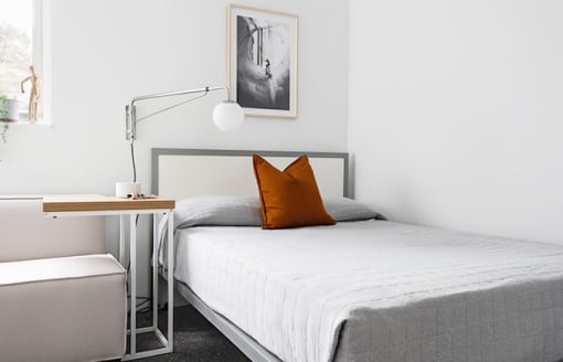 a white bedroom with a bed and a orange pillow