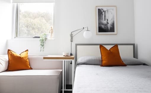 a bedroom with a bed with orange pillows and a window