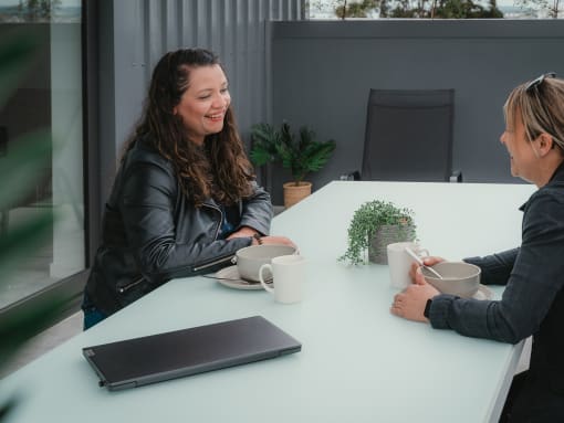 two women sitting at a table drinking coffee and talking