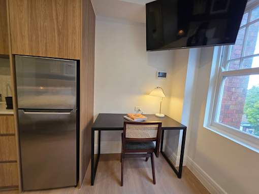 A kitchen with a refrigerator, a table with a chair, and a television mounted on the wall.