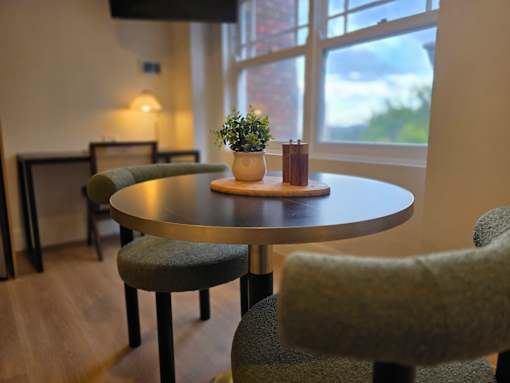 A round table with a potted plant and a candle on it sits in a room with a window in the background.