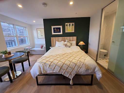 A bedroom with a bed, a chair, a table, and a window.