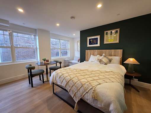 A bedroom with a large bed and a small table with a lamp.