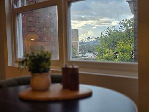 A table with a plant and candle on it in front of a window with a view of a bridge and trees.