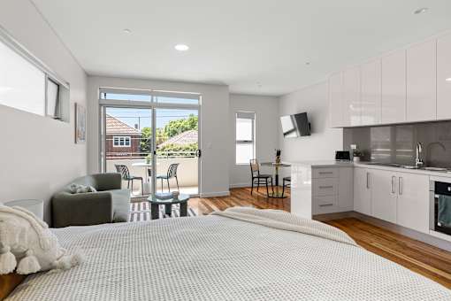 A bedroom with a large bed and a kitchen area in the background.