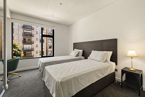 Two beds in a room with a view of a building outside the window.