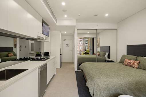 A modern bedroom with a large bed and a kitchen area with a stove.