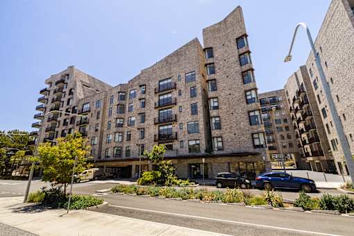 A modern building with curved balconies and a parking lot in front.