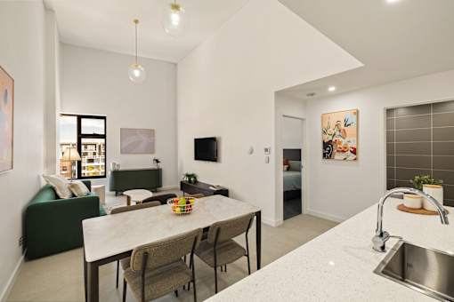 A kitchen with a table and chairs in the foreground and a living room with a couch and television in the background.