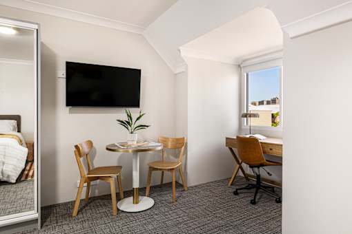 A room with a table, chairs, and a television mounted on the wall.