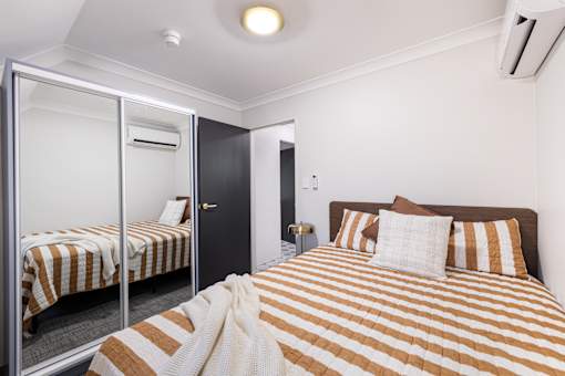 A bedroom with a bed and a mirrored wardrobe.