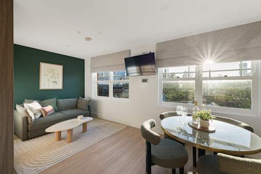 A living room with a grey couch, a glass table, and a television mounted on the wall.