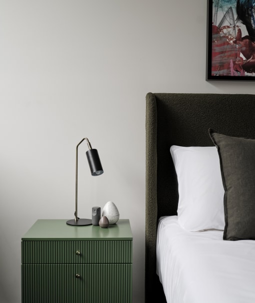 a bedroom with a bed and a green nightstand with a lamp on it