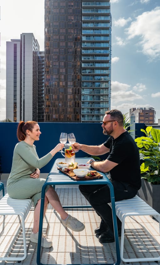 a man and a woman sitting at a table on a balcony drinking wine and eating