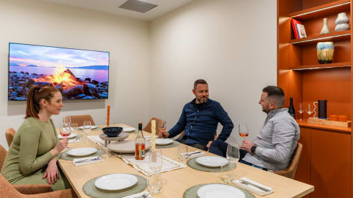 three people sitting around a table drinking wine and watching tv