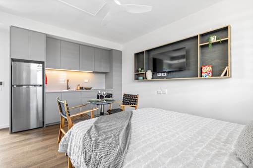 A modern bedroom with a bed, chair, and a kitchen area in the background.