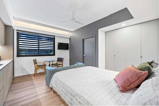 A bedroom with a bed, a chair, a table, and a TV mounted on the wall.