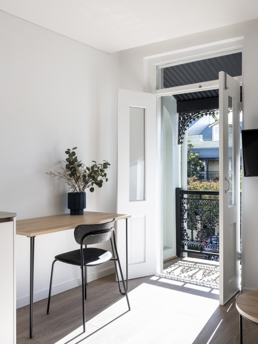 a small table with a black chair in a room with white walls and a staircase