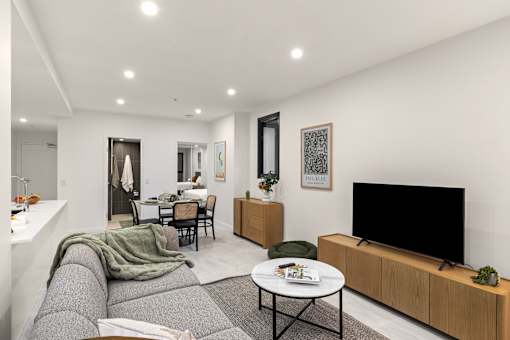 A modern living room with a grey sofa, a black TV, and a dining table with chairs.