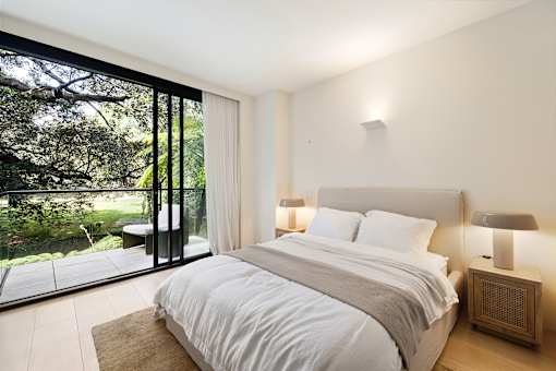 A bedroom with a large bed and a view of the outdoors through a glass door.