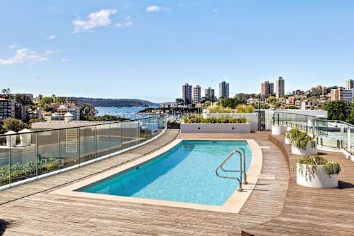 A swimming pool on a wooden deck with a city skyline in the background.