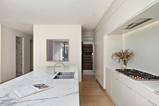 A modern kitchen with a marble countertop and a staircase in the background.